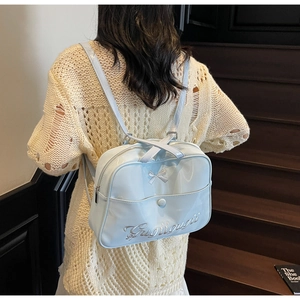 Detail of light blue glossy bow backpack showing metallic ribbon and embroidered text