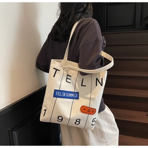 Detail of cream canvas tote bag featuring graphic embroidery and bold letter prints