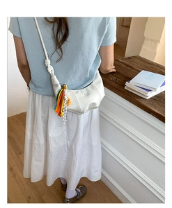 Close-up of a white dumpling crossbody bag with colorful woven charms and a pleated leather texture