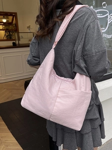 Large light pink nylon tote bag with knot shoulder strap shown on model in cafe