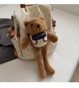 Detail of cream backpack with cartoon bear patterns and a matching plush charm on white surface