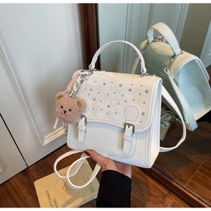 Detail of white faux leather crossbody bag with sparkling rhinestones and a brown bear charm