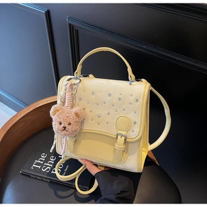 Detail view of yellow crossbody bag with rhinestone flap and plush bear charm