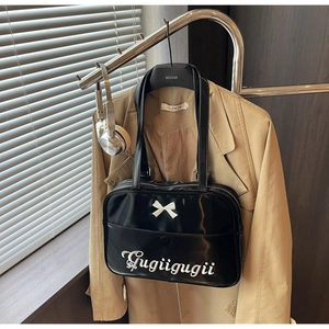 Detail of black glossy shoulder bag with white bow and Gugiigugii lettering in a home setting