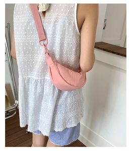 Détail d'un sac demi-lune en nylon rose avec large bandoulière porté par un modèle