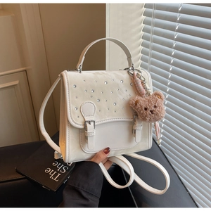 Close-up of white mini backpack with rhinestones, flocking detail and teddy bear charm