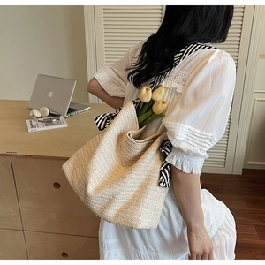 Detailed texture of beige woven straw tote bag with a black and white striped scarf