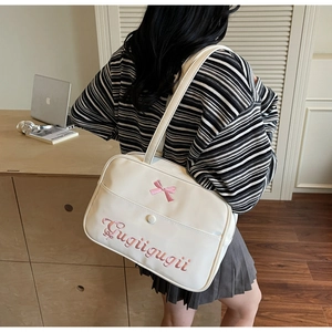 Detail of cream shoulder bag featuring pink bow embroidery and Gugiigugii script lettering