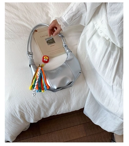Detail of silver crescent bag with textured leather, tassel charm and character pendant
