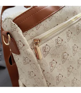 Detailed close-up of smooth golden metal zipper and bear print on stylish cream backpack