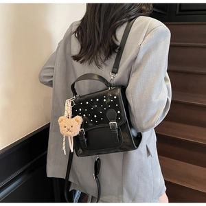 Detail of black faux leather backpack with pearl trim and brown plush bear charm