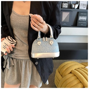 Détail d'un mini sac coquille à paillettes argentées tenu par un mannequin