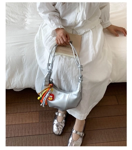 Chic silver crescent hobo bag with colorful tassel charm on a minimalist white bed setting