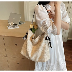 Detail of hand-woven beige straw tote with zebra print strap and striped bow accents