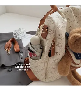 Detail of cream backpack side pocket holding a small folding umbrella with bear charm