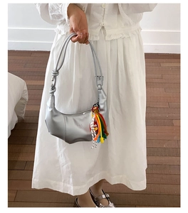 Detail of silver metallic hobo bag featuring a knotted strap and colorful tassel charm