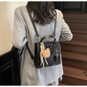 Detail of black leather mini backpack featuring pearl embellishments and teddy bear charm