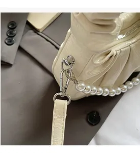 Detail of cream pleated crossbody bag with glossy finish and elegant pearl strap