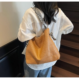 Detail of woven straw tote bag featuring black and white striped shoulder straps for beach use