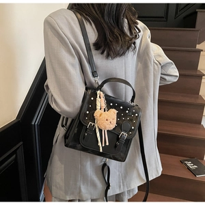 Rear view of a black leather backpack featuring pearl accents and a plush bear charm detail