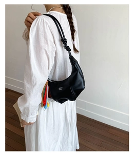 Detail of black crescent hobo bag featuring knotted shoulder strap and colorful tassel charm
