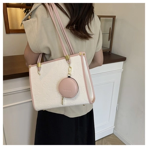 Detail of cream tote bag with pink trim featuring embossed floral patterns and coin purse