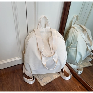 Makro-Detail des weißen Nylon-Rucksacks mit rundem geprägtem Logo und praktischer Seitentasche