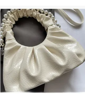 Detailed view of beige pleated leather handbag with elegant pearl handle and gloss finish