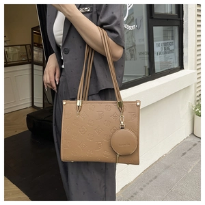 Detail of a brown leather tote bag with embossed clover patterns and a round coin purse charm