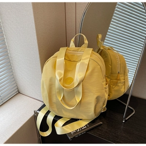 Detailansicht eines gelben Nylonrucksacks mit Griff und rundem Logo auf einem Spiegel