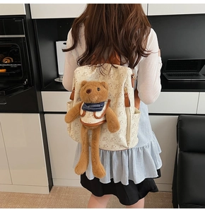 Close-up of a cream-colored floral backpack featuring a plush brown bear doll accessory