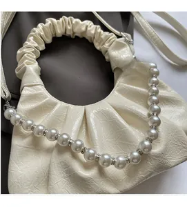 Detailed macro view of cream pleated dumpling bag with pearl handle and rhinestone accents