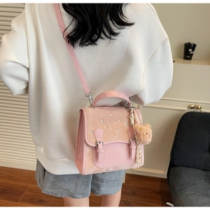 Pink crossbody bag with rhinestones and bear charm shown on a model in a cozy room