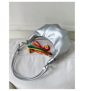 Silver metallic dumpling bag with knotted leather strap and colorful charm on white sofa