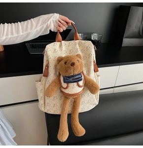 Detail of bear print backpack featuring a large plush bear doll with a blue scarf