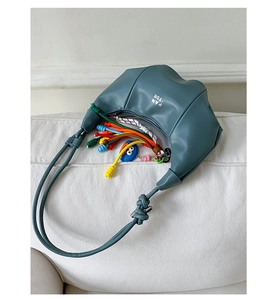 Detail of blue leather crescent bag with colorful woven ropes and a cartoon charm