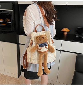 Detailed back view of a beige bear print backpack with brown leather straps and plush charm