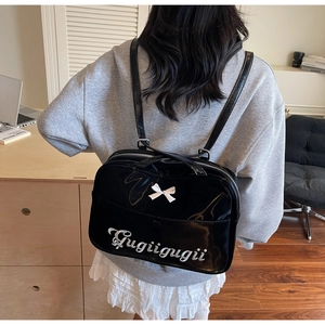 Detail of a black patent leather backpack with white bow and embroidery on a model