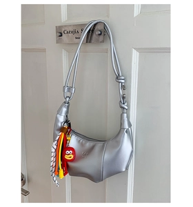 Detail of silver crescent bag featuring PAN TOR embossing and decorative cartoon pendant