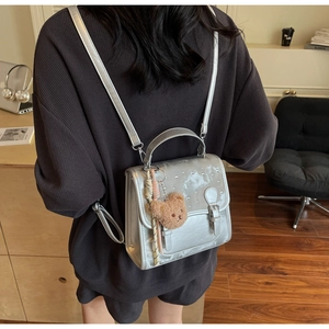 Silver rhinestone backpack with plush bear charm worn by a model in a cozy indoor setting