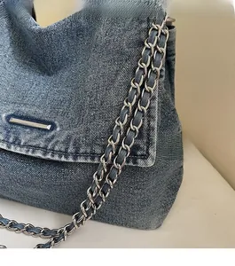 Close-up of blue denim flap bag with metal chain strap and decorative silver hardware