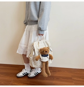Side view of a cream backpack with bear prints and a 3D plush bear charm on a model