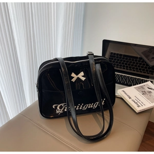 Detail of black patent leather shoulder bag with white 3D bow and logo embroidery