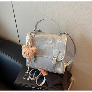 Detail of silver metallic handbag with crystal studs and a plush bear charm on books