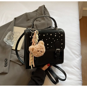Detail of black faux leather backpack with silver studs and cute plush bear charm