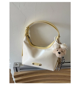 Detailed view of cream leather tote bag with yellow trim and cute plush dog charm
