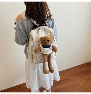 Detail of white printed backpack with cute brown plush bear charm and side pocket view