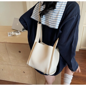 Detail of white lychee leather bucket bag with gold studs on a minimalist desk