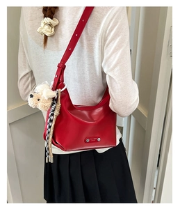 Detailed view of red hobo bag with plush puppy charm and metal tassel on white shirt