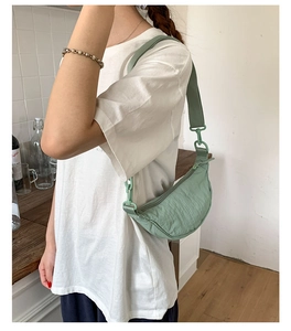 Gros plan d'un sac demi-lune en nylon vert clair plissé porté sur l'épaule du mannequin